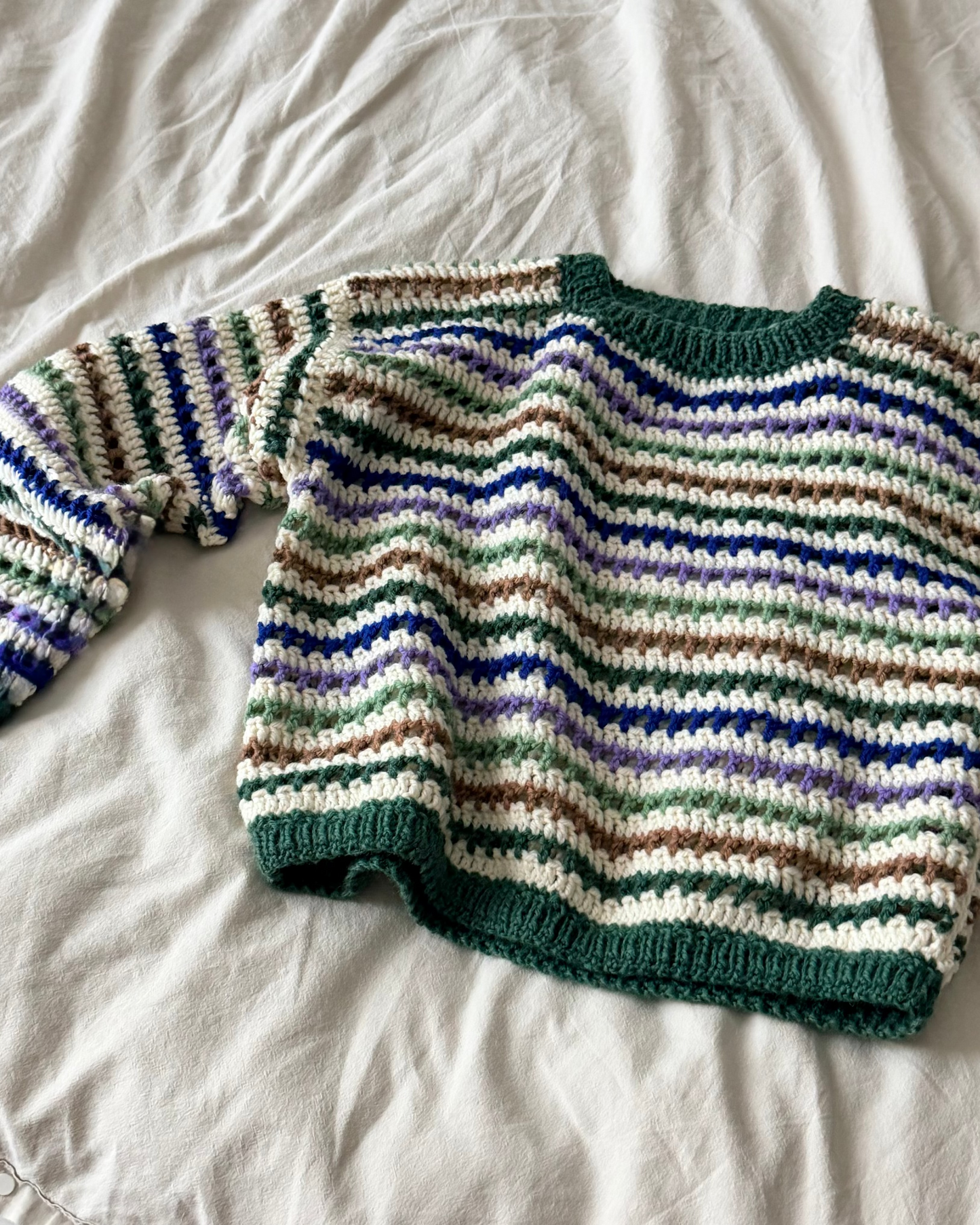 Striped sweater with green, blue, and brown pattern on a white fabric background