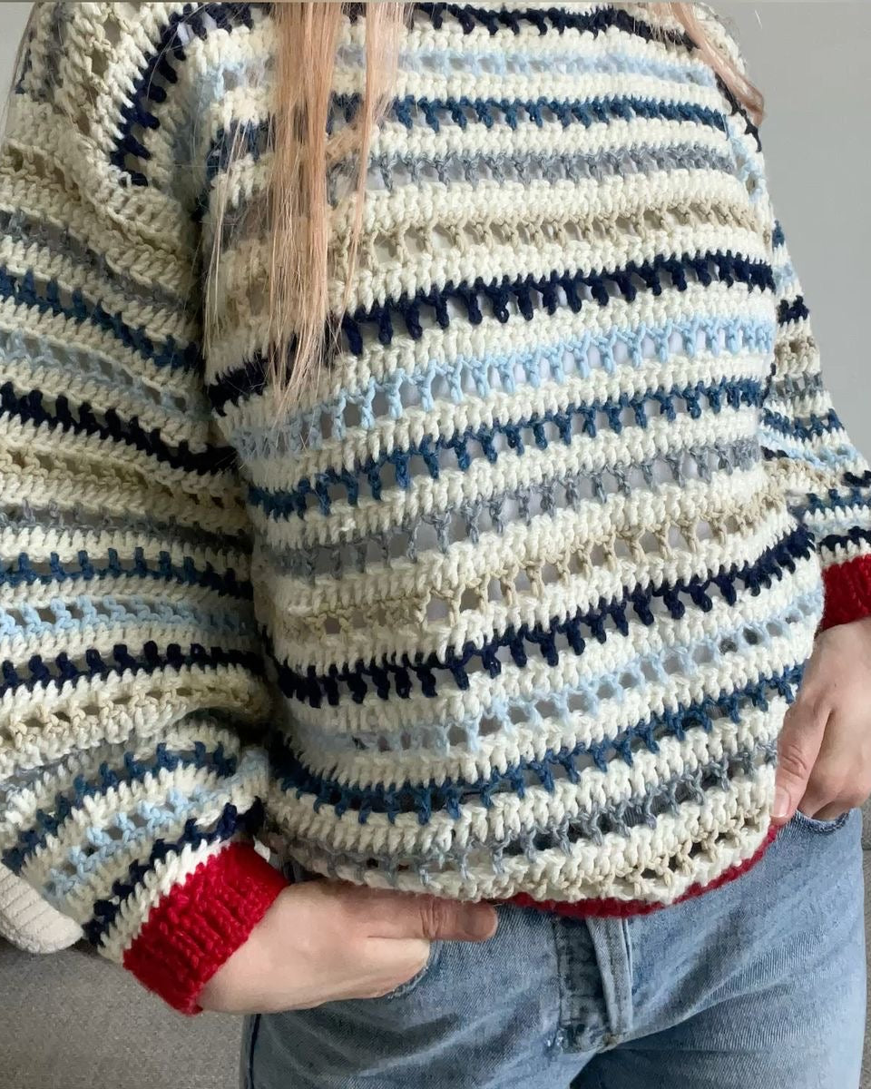 Person wearing a striped crochet sweater with red cuffs and trim.