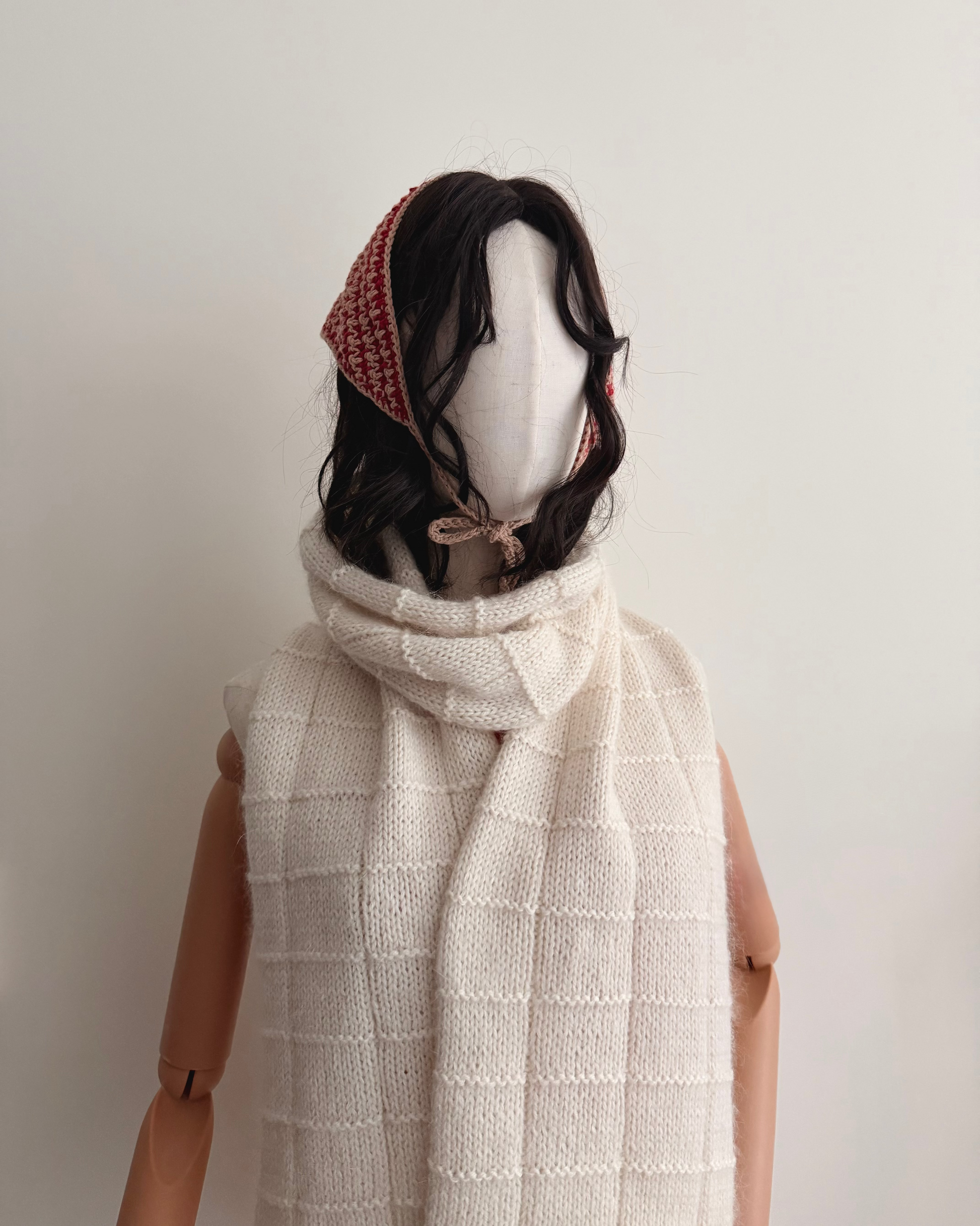 Mannequin wearing a white scarf and red headband against a plain background