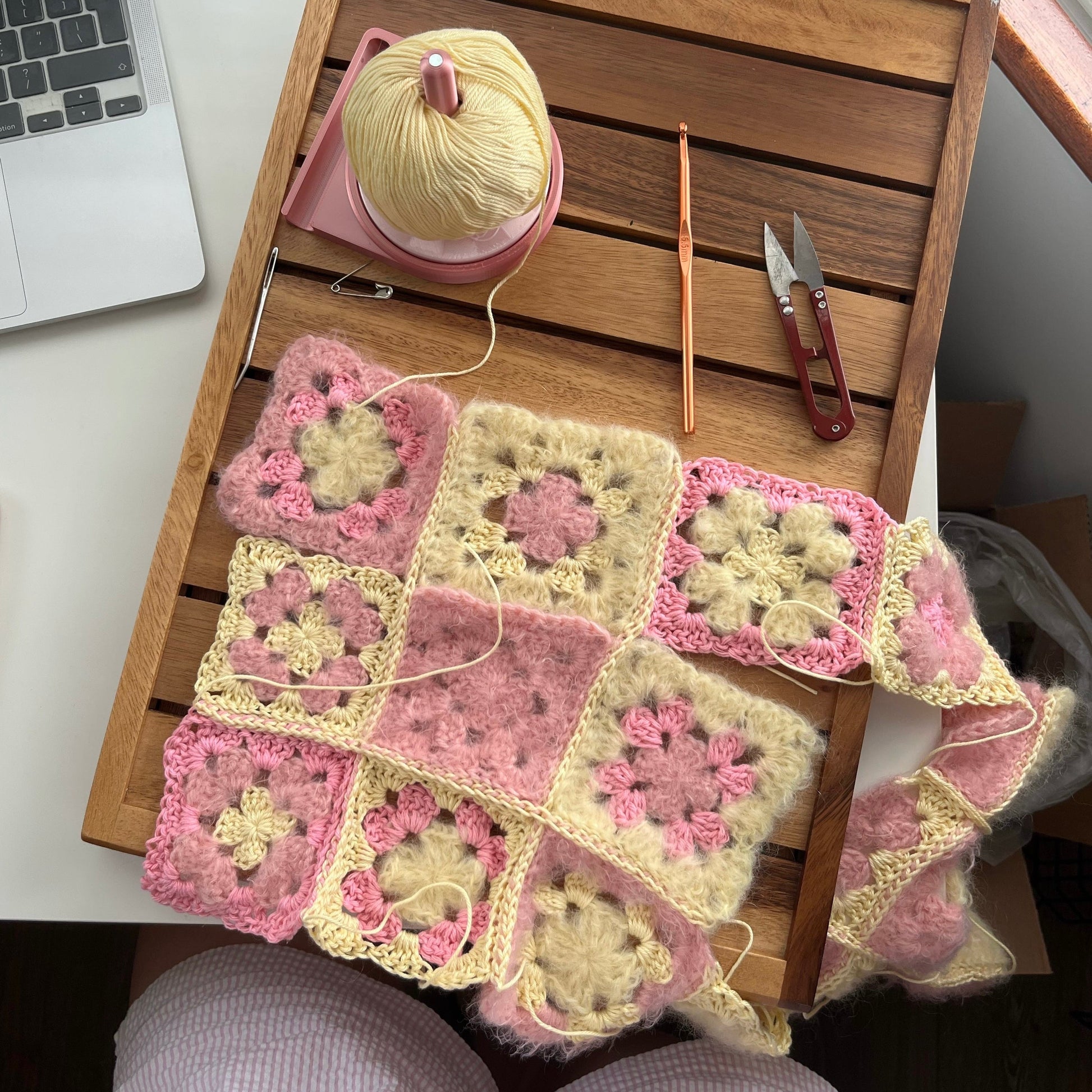 Crocheted squares on a wooden table with yarn and tools