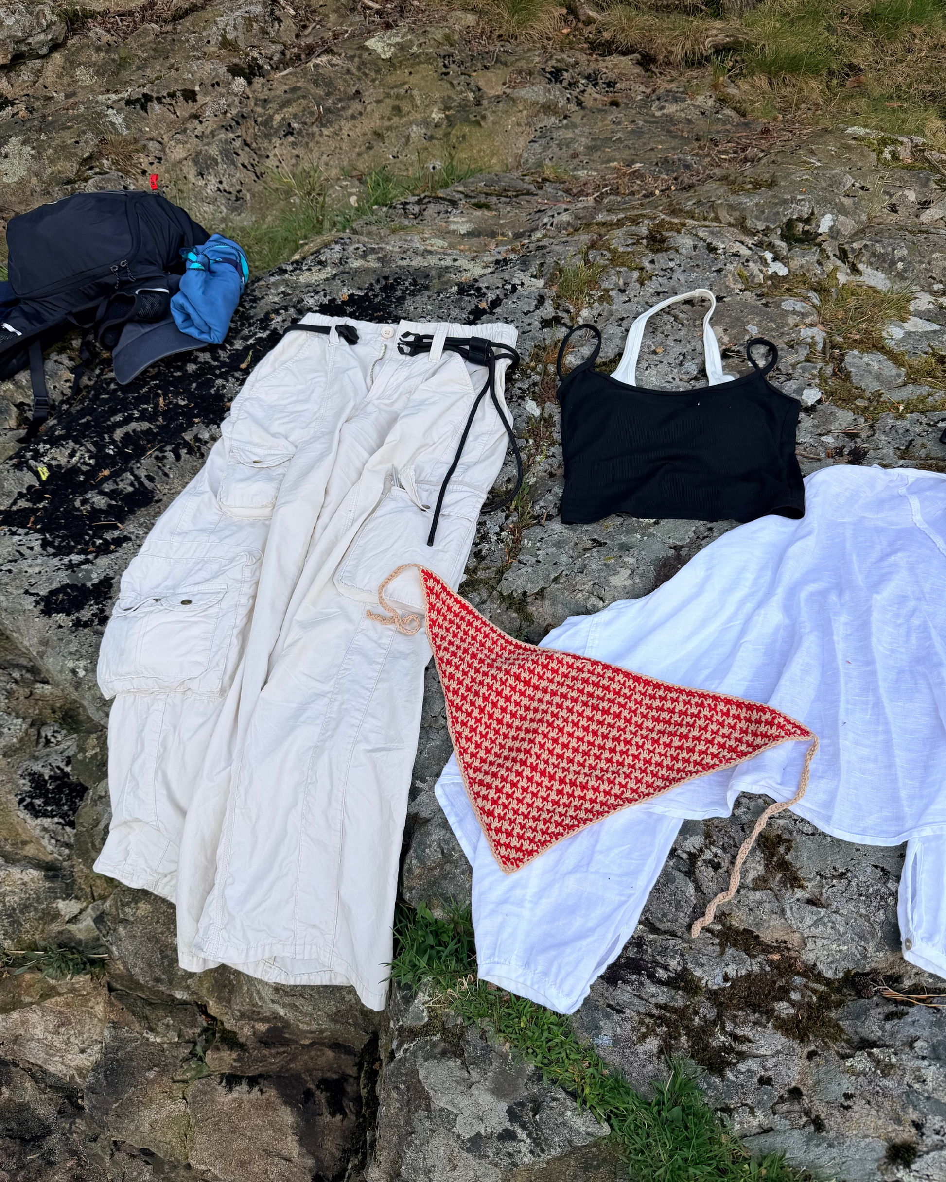 Clothing items including a white jacket, black swimsuit, and red and white patterned towel on a rocky surface.