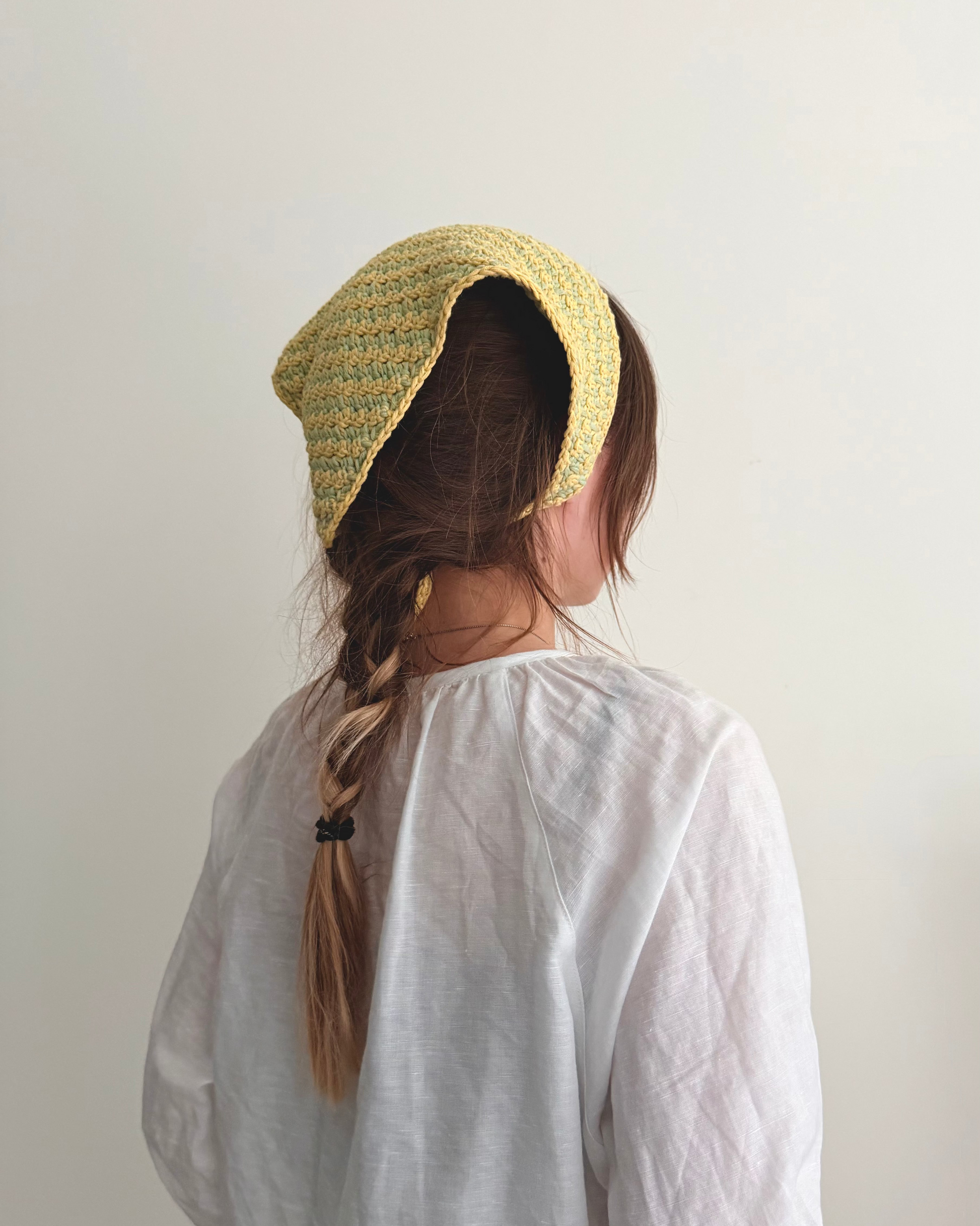 Person wearing a yellow knitted bonnet and white shirt against a plain background