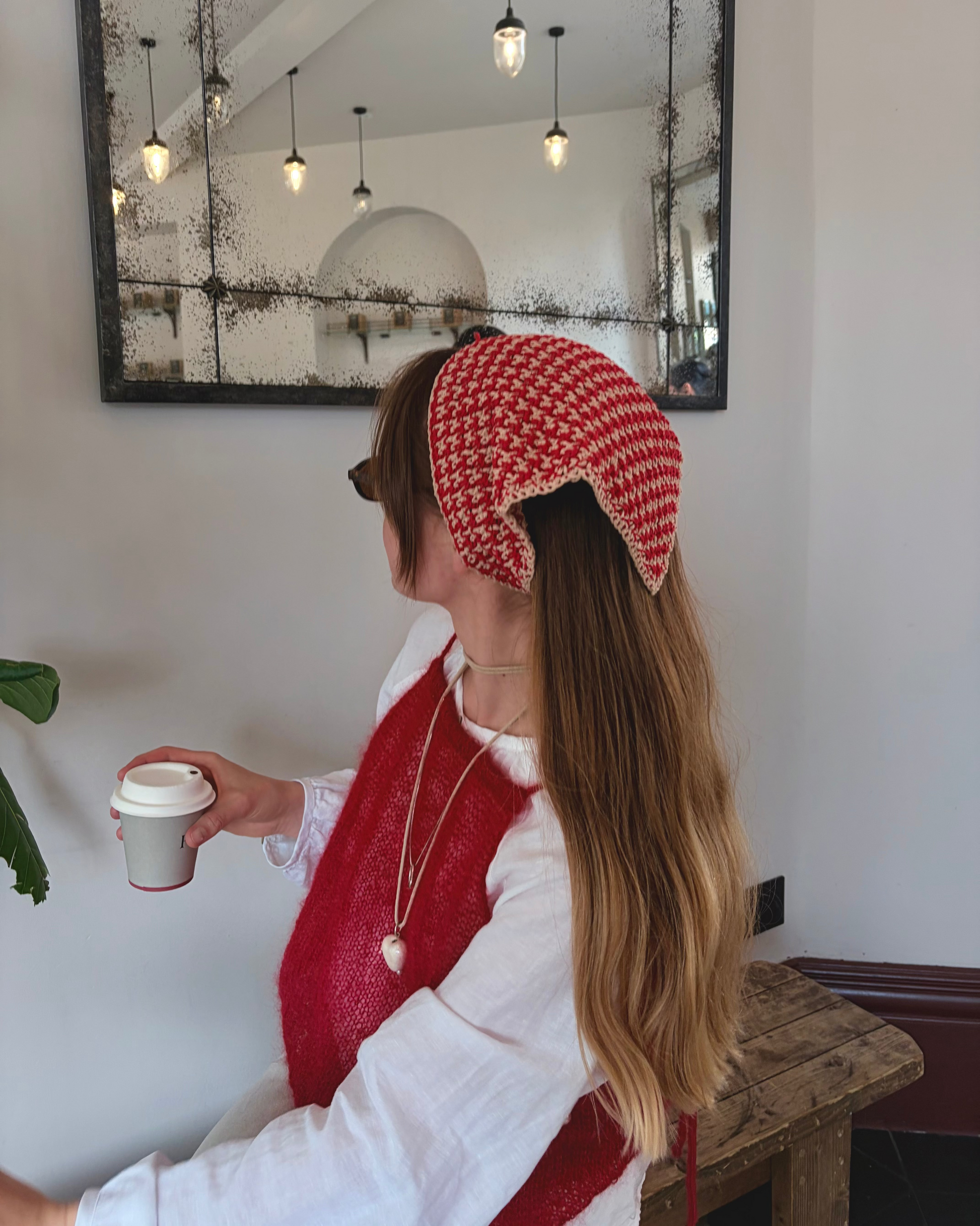 Woman wearing a red and white patterned headband, red scarf, and white shirt in a room with a mirror on the wall.