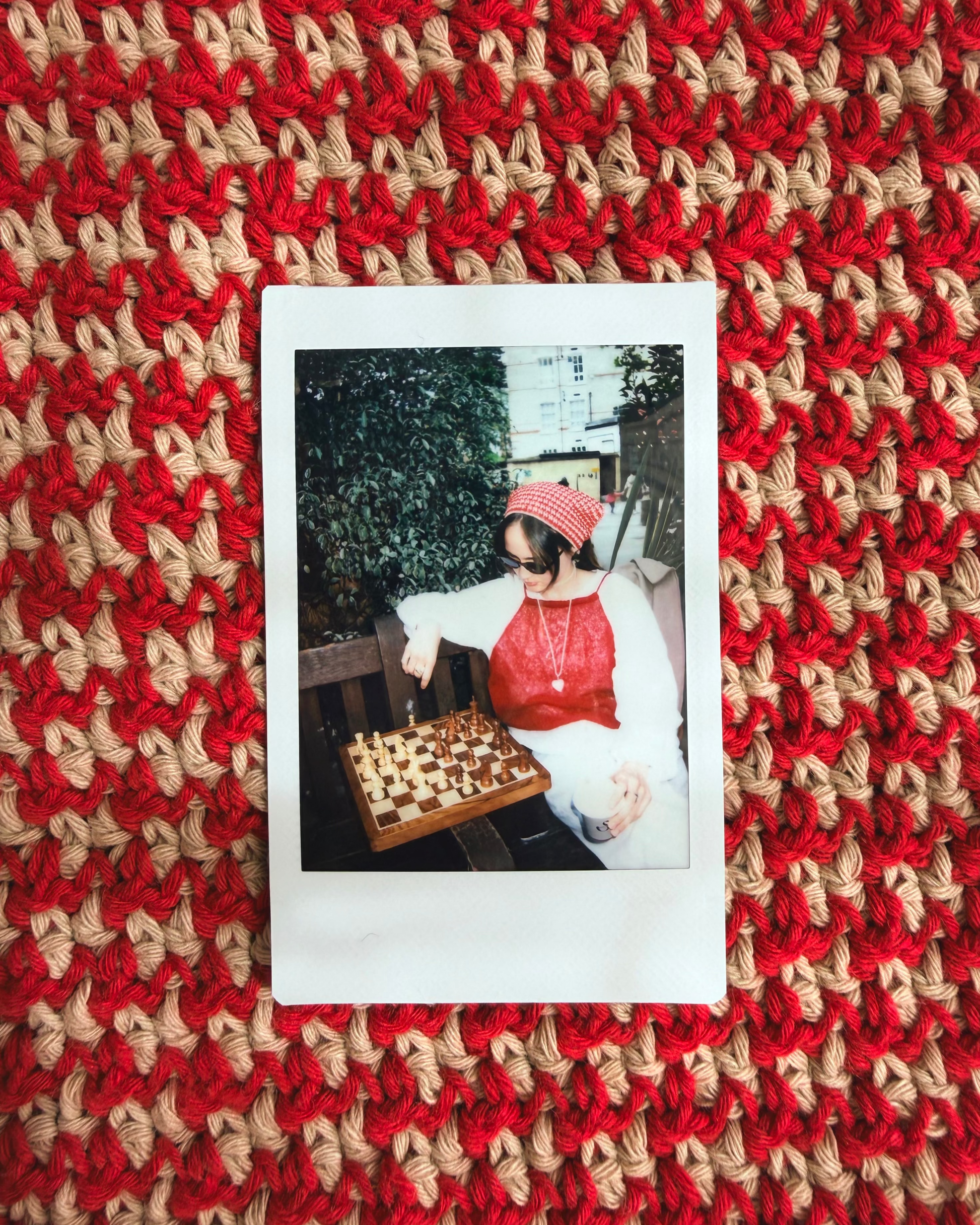 Polaroid photo of a person with a red scarf on a red and beige textured fabric background